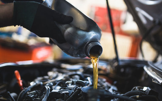 An individual wearing black gloves while pouring amber-colored liquid into a black funnel placed in a car engine.