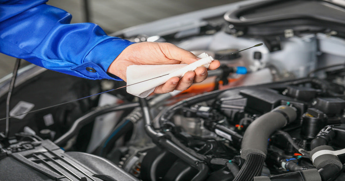 A close-up of a person in a blue shirt using a dipstick and a paper towel to check the oil level in a car engine.