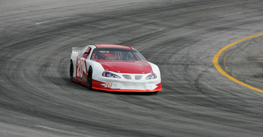 A red and white race car with the number "20" on the front bumper and passenger side door driving on a track.