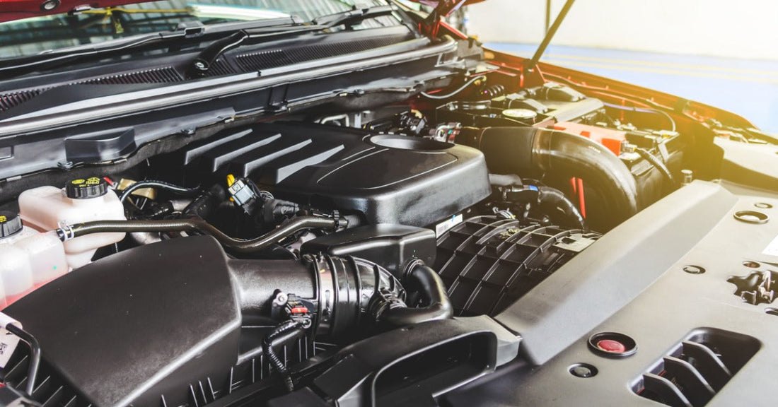 Open hood of a red car reveals a clean engine bay with black engine cover, air intake, hoses, and coolant reservoir.