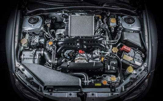 Open car engine bay with visible intercooler, battery, hoses, fluid reservoirs, and other mechanical components.