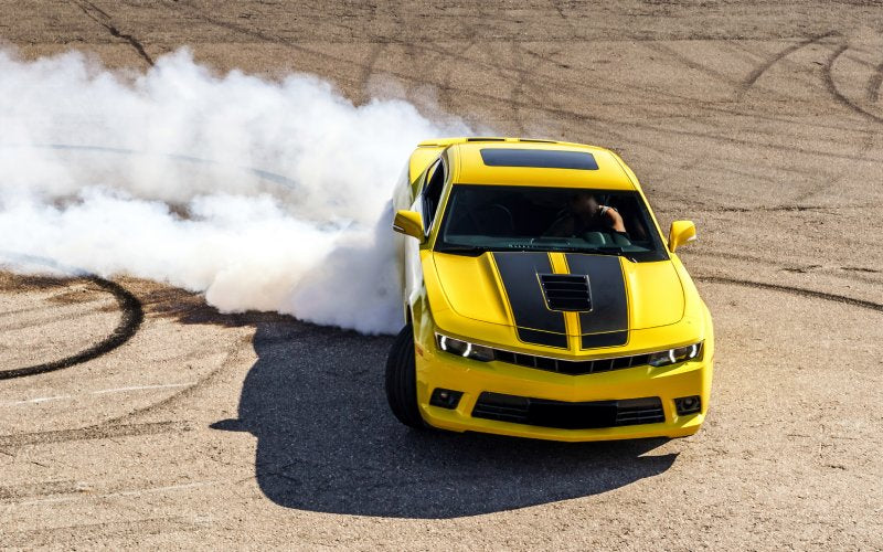 A yellow and black sports car producing a large plume of smoke while driving on a road with black tire marks.