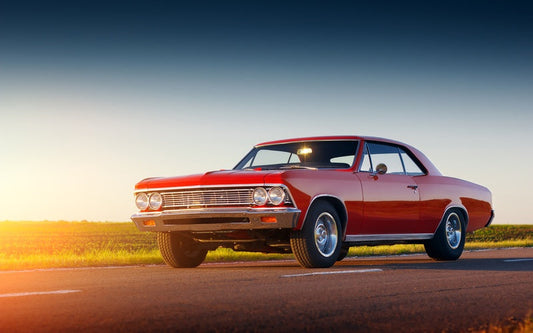 A red two-door classic car with chrome accents parked on an asphalt road. The light from sunset is reflecting off the car.