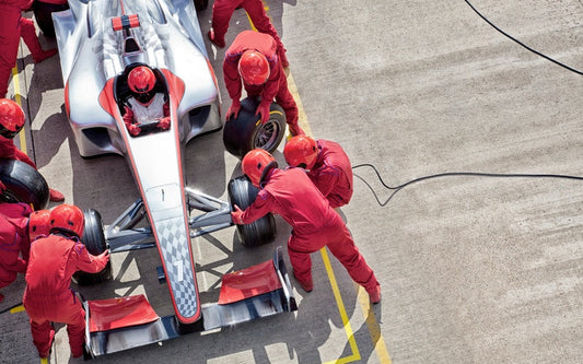 An aerial view of a crew team in red uniforms and helmets changing the tires on a red and silver race car.