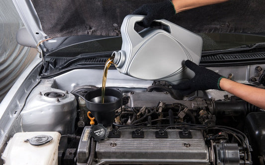 An individual wearing black gloves using a black funnel to pour amber-colored oil into a vehicle engine.