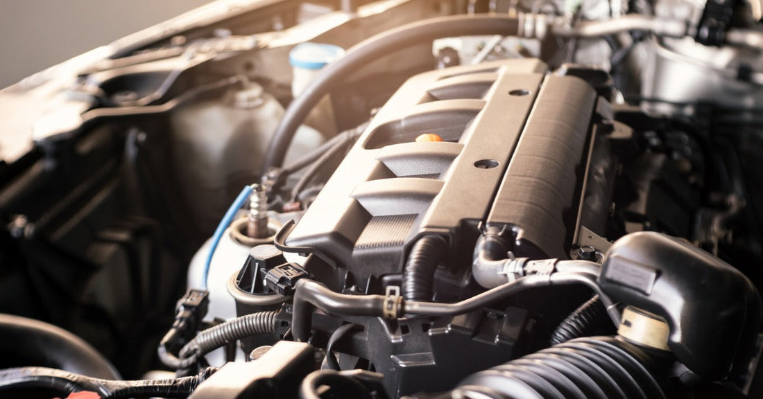 Close-up of a modern car engine inside the engine bay, showing the engine cover, hoses, wiring, and intake components.