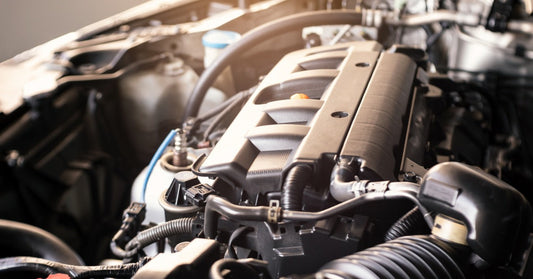 Close-up of a modern car engine inside the engine bay, showing the engine cover, hoses, wiring, and intake components.