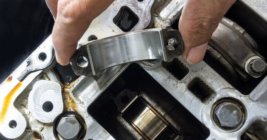 An auto mechanic's hand picking up a piece of a car's engine before replacing it with a new replacement part.